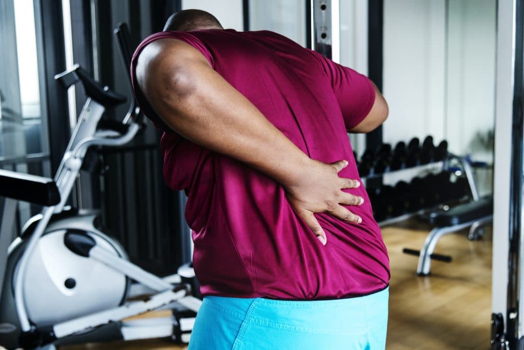 man in the gym holding his upper back due to pain