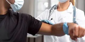 female chiropractor with medical mask and gloves checking mans elbow pain
